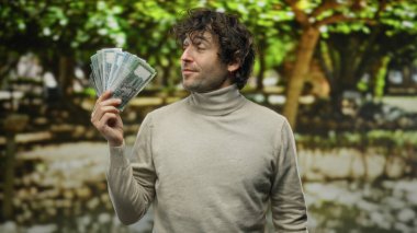 Bangladeş 'i tutan İspanyol bir adam arka planda ağaçların bulanıklaştığı bir park ortamında doğal bir çevrede zenginlik ve eğlence tasvir ediyor..