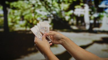 Güneşli bir şehir parkının bulanık arka planına karşı ellerinde Singapur banknotları tutan adam, açık hava planlama kavramını somutlaştırıyor..