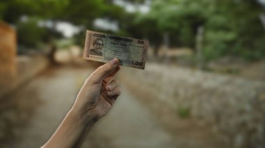Canlı bir açık hava parkında bangladeş banknotunu tutan bir adam Taka 'yı yemyeşil bir arka planda sergiliyor..