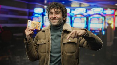 İspanyol adam kumarhanenin içinde kumar makineleriyle avro banknotunu tutarken, Avrupa 'nın iç mekanlarında heyecan ve beklenti ortamı yaratıyor..