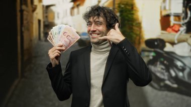 Şehir sokaklarında yaşayan İspanyol bir adam, Thai Baht banknotlarını tutarken, finans temalarını somutlaştırırken ve şehir içinde gezerken bir telefon jesti yapıyor..