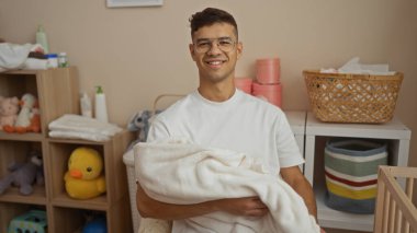 Genç bir adam oyuncaklar ve depo sepetleriyle çevrili rahat bir çocuk odasında, evde huzurlu bir aile ortamının altını çiziyor..