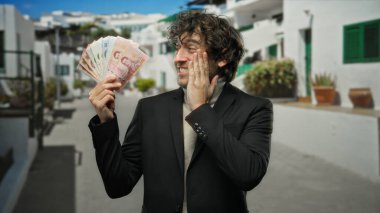 Şehir sokaklarında renkli banknotlar tutan bir adam, heyecan ve finansal başarı ifadesiyle Tayland paralarını sergiliyor..