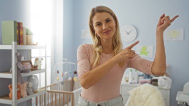 Yatak odasında gülümseyen bir kadın, rahat ev ortamında günlük giysiler giyen sarışın bir kadın bebek oyuncakları ve parlak gündüz dekoruyla..