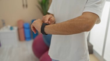 Spor salonundaki genç adam spor aletlerinin yanında spor aletlerini kontrol ediyor. Bu da yetişkin spor meraklıları için spor salonunda teknik kullanım anlamına geliyor.