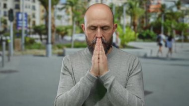 Şehir sokağında elleri ve gözleri kapalı meditasyon yapan bulanık insanlar arka planda palmiye ağaçları, kel ve sakallı gri kazaklar giyen bir adam..