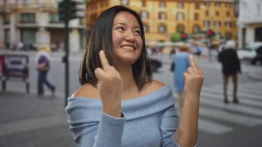 Şehirli bir sokakta neşeli bir jest yaparken gülümseyen bir kadın. Bulanık bir arka plan ve uzaklarda yürüyen insanlar..