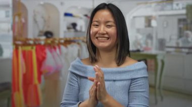 Canlı bir perakende mağazasında gülümseyen bir kadın renkli giysilerle karşılama mağazasında el çırpıyor..