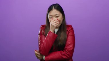 Kırmızı ceketli bir kadın gülüyor, ağzı kapalı, mor arka planda neşeli duygular besliyor, çekici bir moda..