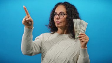 Gözlüklü kadın, Amerikan doları banknotlarını ve parlak mavi duvara karşı bırakılan puanları elinde tutuyor. Kendine güvenen ifadesiyle zenginlik ve karar verme yeteneği sergiliyor..