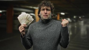 Otoparkta Rus rublesi tutan İspanyol bir adam. Gri kazak giyen, ekonomik stresi sembolize eden yumruklarıyla hayal kırıklığını gösteriyor..