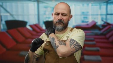 Dövmeli bir adam yolcu gemisinde boynu ovuyor, rahatsızlık gösteriyor, modern şezlonglarla çevrili, günlük kıyafetler giymiş, açık hava ortamını vurguluyor..