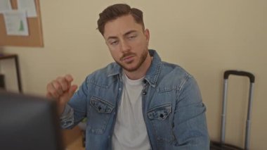 Ofis ortamında sakallı genç bir adam kot ceket giyerken ve modern bir iş yerinde masa başında otururken parmaklarıyla hareket eder..