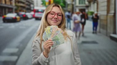 Gözlüklü, gülümseyen ve elinde Romanya parası olan genç bir kadın kalabalık bir şehir caddesinde zenginlik ve şehir yaşamını harmanlayan canlı bir sahne yaratıyor..