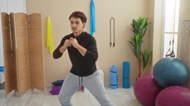 Spor salonunda egzersiz yapan genç bir adam. Etrafı spor aletleriyle çevrili. Duruşuna ve konsantrasyonuna odaklanmış..