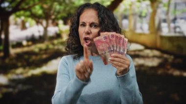 Orta yaşlı bir kadın parkın dışında, elinde Güney Afrika banknotları tutuyordu. Sinirli bir şekilde parmaklarıyla hareket ediyordu. Doğal bir bahçe ortamında anlaşmazlıklarını dile getiriyordu..