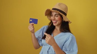 Sarı arka planda bir şapka takmış, kredi kartıyla gülümseyen bir kadın heyecan ve neşe gösteriyor.