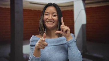 Çinli bir kadın, neşeli bir ifade ve rahat bir duruş ile bir inşaat alanında neşeli bir şekilde el kol hareketi yaparak, neşeli bir etkileşim anını yakalıyor..