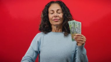 Kadın, Avustralya doları ile izole edilmiş kırmızı arka planda meditasyon yapıyor. Orta yaşlı, rahat bir kadın elinde banknotlar tutuyor..