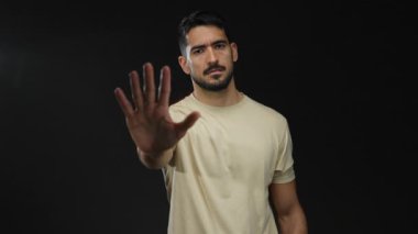 Genç ispanyol adam, izole edilmiş siyah bir arkaplan üzerinde parmağıyla onaylamadığını işaret ediyor.