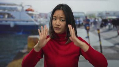 Kırmızılı genç kadın sakin bir jest yapıyor. Yoğun bir günde arka planda teknesi olan deniz kenarında.