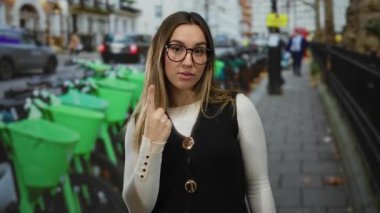 Dışarıda kutlayan genç bir kadın kalabalık bir caddede, bisikletlerle ve şehir hayatıyla çevrili, heyecan ve hareketlilik gösteren jestlerle..