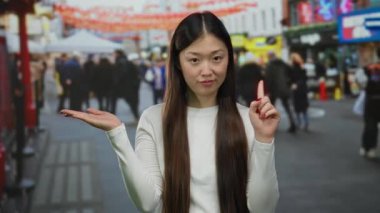 Hayır diyen bir kadın, arka planda canlı şehir hayatı ve kültürel unsurlarla çevrili, Çin 'deki işlek şehir caddesinde açık avuçla işaret ediyor..