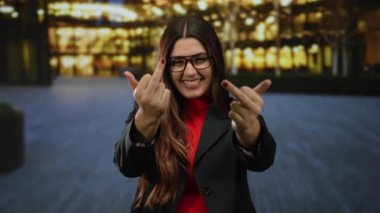 Açık havada gülümseyen İspanyol kadın gece aydınlanmış şehir caddesinde kaba bir jest yapıyor..