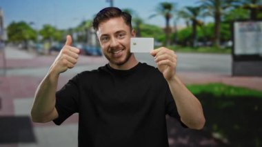 Şehir merkezindeki açık hava ortamının ortasındaki finansal başarıyı sembolize eden kredi kartı tutan genç bir adam..