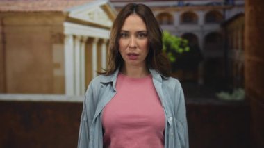 Latin kökenli genç bir kadın, eski bir üniversite binasında, tarihi bir mimari geçmişe karşı kendine güvenen bir ifade sergiliyor..