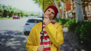 Sarı yağmurluklu İspanyol adam, şehir caddesinde nazikçe olta tutuyor, modern yaşam ve geleneksel aktivitenin karışımını somutlaştırıyor..