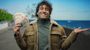 İspanyol adam elinde Türk lira banknotları tutarak gülümsüyor güneşli sahil arka planında, mutluluğu ve açık havada eğlenmeyi ifade ediyor..