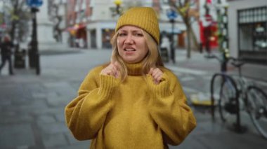 Sarı kazaklı kadın, arka planda bisikletleri olan şehir sokaklarında tiksinerek tepki veriyor..