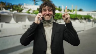 Genç adam şehir dışında telefonla konuşurken yukarıyı işaret ediyor. Gün boyunca gülümsüyor. Kendine güveniyor..