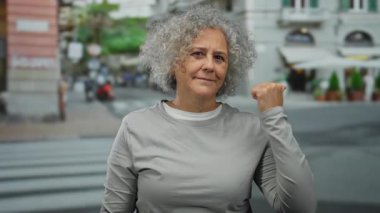 Kıvırcık saçlı, kendinden emin orta yaşlı kadın sokak ortamında dikiliyor, güç gösterisi yapıyor ve bağımsızlığını ilan ediyor..