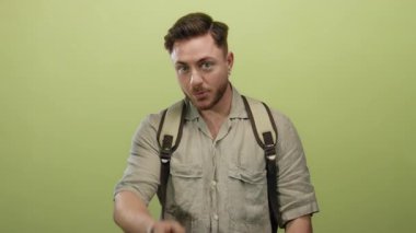 Sakallı ve sırt çantalı genç bir adam, izole edilmiş sarı bir arka planda kameraya özgüvenle ve bir gezginin ruhuyla işaret ederek beni çağırıyor..