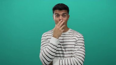 Çizgili genç adam yeşil arka plana şaşırmış görünüyor, izole edilmiş bir portre ortamında gizemli bir şekilde modern ve temiz bir stil sergiliyor..