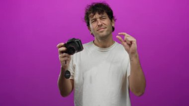 İspanyol adam, fotoğraf çekiminde odak ve yaratıcılığını ifade ederek, canlı pembe bir arka plana karşı kamerayla küçük bir şey tutarken el kol hareketi yapıyor..