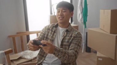 Yeni evde video oyunları oynayan genç bir adam. Parlak bir oturma odasında, yeni bir başlangıç ve boş zamanı tasvir eden kutularla çevrili..