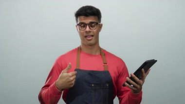 Gözlüklü ve önlüklü genç adam tableti tutarken gülümsüyor ve beyaz arka plana başparmak işareti yapıyor.