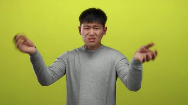 Elleri havada duygularını ifade eden genç bir adam izole edilmiş sarı arka plan üzerinde günlük gri süveter giyiyor..