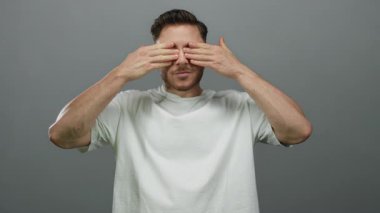 Sakallı ve gözleri açık genç bir adam izole edilmiş gri arka plana karşı şaşkınlık içinde duygularını ve merakını ifade ediyor..