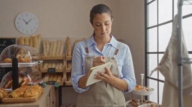 Fırında çalışan genç bir kadın arka planda çeşitli hamur işleri ve ekmeklerle notlar alıyor, samimi ve davetkar bir ortam yaratıyor.