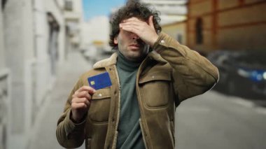 İspanyol asıllı bir adam şehrin arka planına karşı stresli ve mali kaygılarını gösteren bir kredi kartını kentte tutarken sinirli görünüyor..