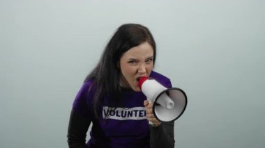 Esmer saçlı bir kadın gönüllü gömleğiyle megafonu tutkulu bir şekilde gri bir arkaplana, canlı bir ifadeye ve toplumsal nişana karşı kullanıyor..