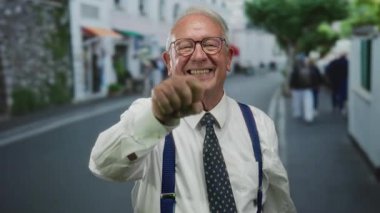 İş kıyafeti giymiş kıdemli bir adam canlı bir sokakta gülümsüyor, kendine güven ve pozitiflik yayıyor, açık bir şehir arkaplanı var, izleyiciyle meşgul..