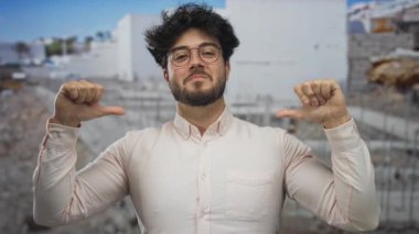 Sakallı, gözlüklü, gülümseyen ve bir inşaat alanında kendini gösteren genç bir adam, günlük kıyafetlere olan güvenini dile getiriyor..