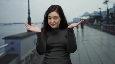 Kumsal zemininde gezinen bir kadın bulutlu bir günde düşünceli bir yüz ifadesi sergiliyor. Kumral saçlarını ve sakin bir kıyı ortamında günlük kıyafetlerini vurguluyor..