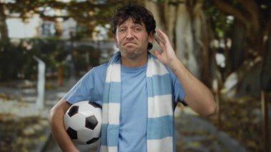 Futbolcu İspanyol bir adam, bir spor müsabakası sırasında mavi gömlek ve çizgili eşarp giyen yemyeşil bir parkın içinde hayal kırıklığını ifade ediyor..