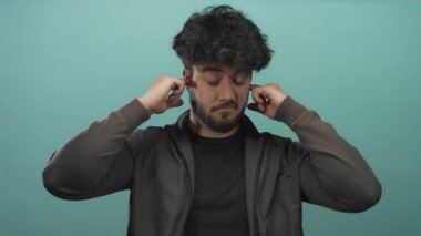 Giyim kuşamında sakallı genç adam gözleri kapalı kulakları kulaklarında yeşil arka planda gürültü veya stresi engelleme hissi taşıyor..